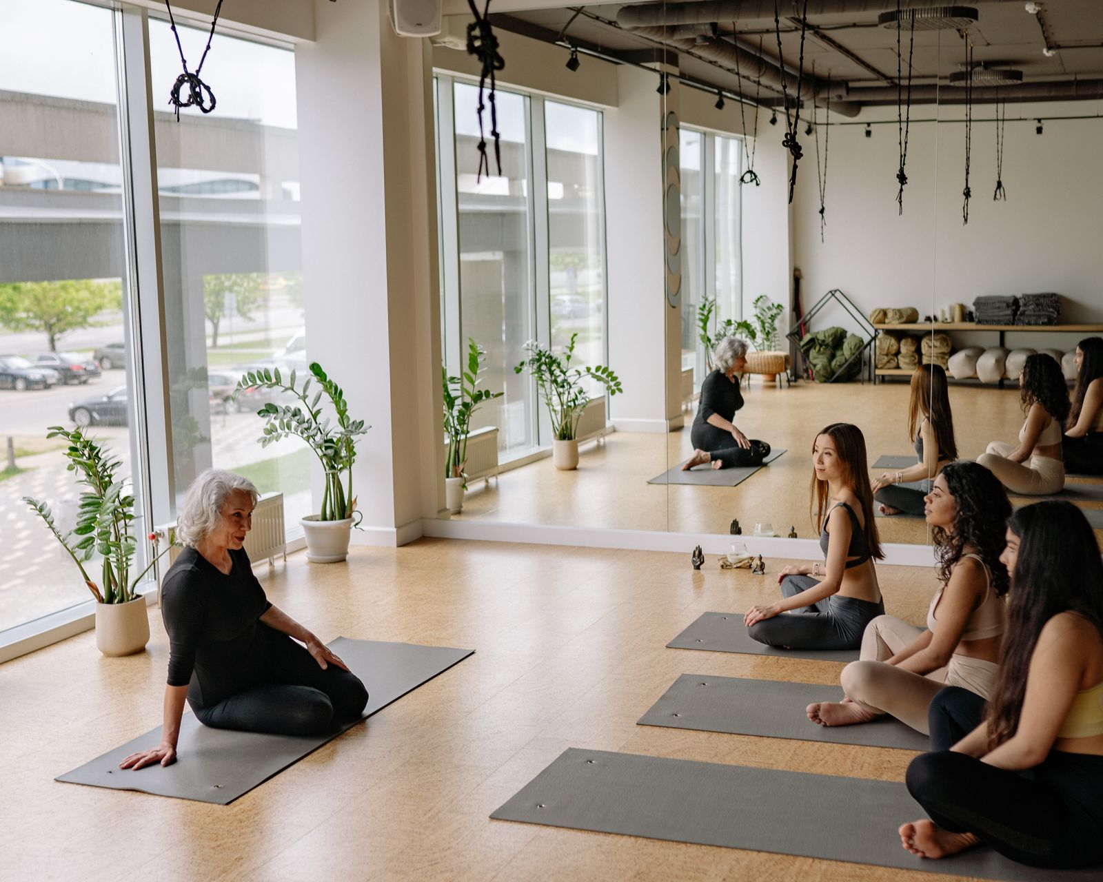 A yoga class seated on mats in a bright studio with plants and mirrors
