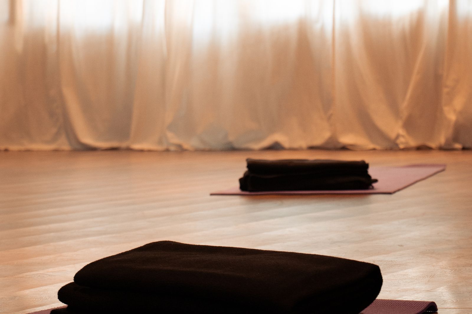 A quiet yoga room with warm curtains and a folded blanket on a mat