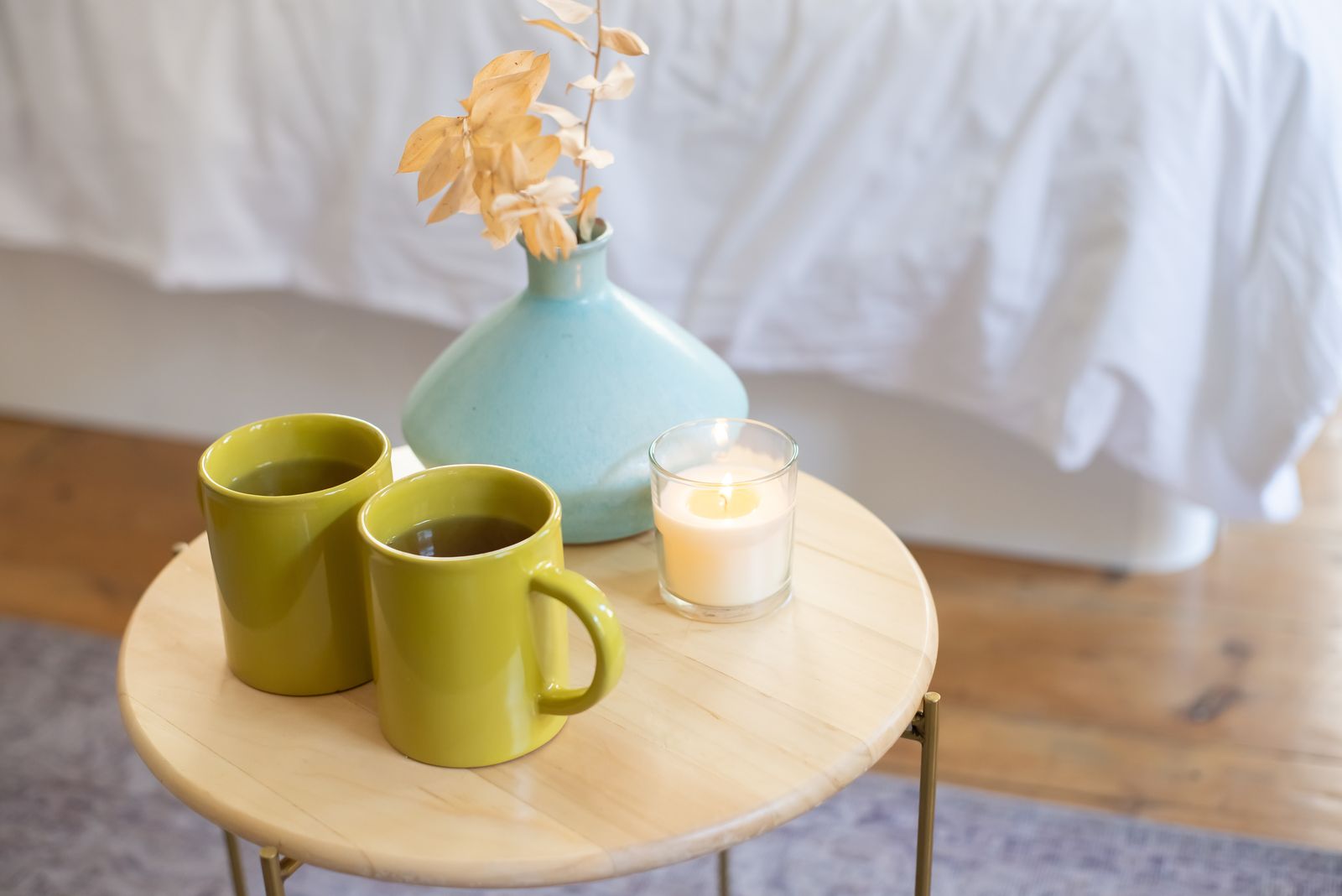 Two green mugs of tea and a candle on a small wooden table