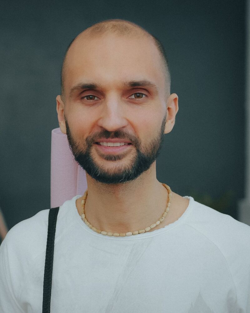Daniel Marsh, bearded and bald, smiling in the studio with a mat strap over his shoulder