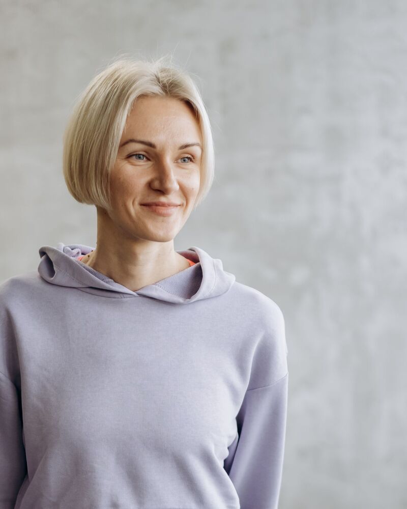 Lena Whitfield, with a short blonde bob, standing in a gray hooded sweatshirt against a concrete wall